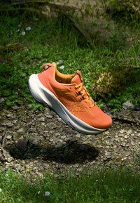 Orange athletic shoe with a textured upper, contrasting white midsole, and black accents. Features laces and a pull tab on the heel.