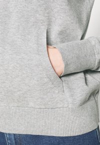 Szara bluza z miękkiego materiału, z prążkowanym dołem i mankietami, z widoczną boczną kieszenią na przodzie.