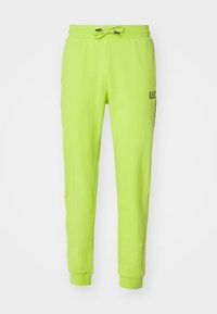Jasně neonově zelené tepláky s elastickým pasem, stahovací šňůrkou, manžetami na kotnících a malým černým logem EA7 Emporio Armani na pravém stehně.