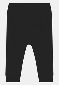 Svarta joggers tillverkade av mjuk tyg, med elastisk midja, smalnande ben och en bakficka. Slät textur utan mönster.