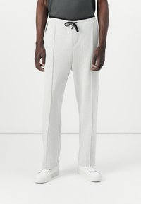Light gray sweatpants with a textured finish, drawstring waist, front pockets, and tapered legs. Paired with white sneakers.