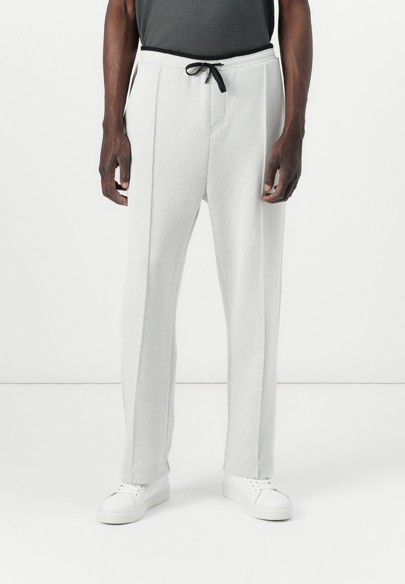 Light gray sweatpants with a textured finish, drawstring waist, front pockets, and tapered legs. Paired with white sneakers.