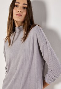 Pull col roulé en maille côtelée gris clair, à manches longues, avec un tissu texturé et une coupe décontractée, souligné par un col haut.