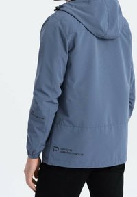 Giacca con cappuccio blu realizzata in tessuto leggero. Presenta polsini elasticizzati, dettagli con logo sulla manica e un design semplice e aerodinamico.