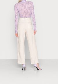 Haut à manches longues en maille violette avec motif floral, associé à un pantalon large en lin beige. Chaussures à talons blocs transparents.