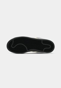 Šedá podrážka sneakers s čiernou, textúrovanou gumou s cik-cak vzorom, doplnená žltými pruhmi na hornej strane.