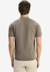 Kortärmad polotröja i dämpad beige med ett texturerat mönster samt ribbad krage och fåll, sedd bakifrån.