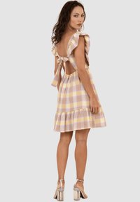 Vestido a cuadros en amarillo pastel, rosa y blanco, con mangas con volantes, corte en la espalda y un lazo atado, que presenta una falda acampanada con un dobladillo en capas.