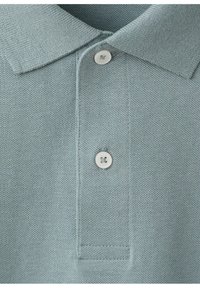 Polo tricoté bleu clair avec deux boutons blancs et un col classique, montrant le détail du tissu texturé.
