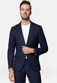 Nocnoniebieska marynarka w delikatny wzór w kratę, dopasowany krój, klapy notch oraz dwie przednie kieszenie. Noszona na białym T-shircie.