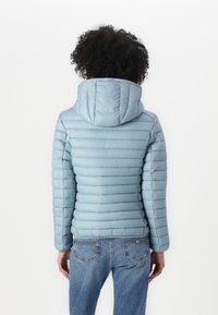 Lichtblauwe pufferjack met horizontale stiksels, een capuchon en aansluitende mouwen. Draag het met een blauwe spijkerbroek, vanuit de achterkant gezien.