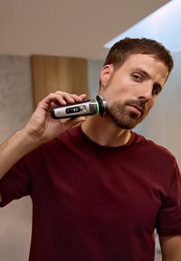 Elektrisch aangedreven scheerapparaat met een zilver- en zwart ontwerp. Heeft een display dat tijd en batterij toont, met een groene LED-accent.