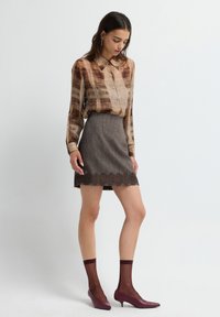 Blusa marrone a fantasia con maniche lunghe e bottoni abbinata a una gonna grigia con orlo in pizzo. Indossata con tacchi bordeaux e calze.
