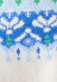 Tessuto di maglione lavorato a maglia con un motivo di fiocchi di neve blu e bianchi con accenti verdi. Texture morbida e pelosa; sfondo crema.