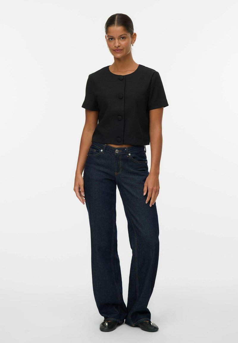 Svart kort topp med rund halsringning och korta ärmar, med tre stora knappar. Kombinerad med mörkblå raka jeans.