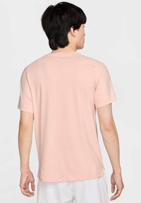 Camiseta corta de manga corta en rosa claro, hecha de tela texturizada. Presenta un cuello redondo y aberturas en los laterales del dobladillo para un ajuste relajado.