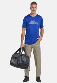 Blauw sport t-shirt met berggraphic, beige cargobroek en zwart/grijze sporttas met logo. Lichtgewicht, casual ontwerp, praktisch voor buitengebruik.