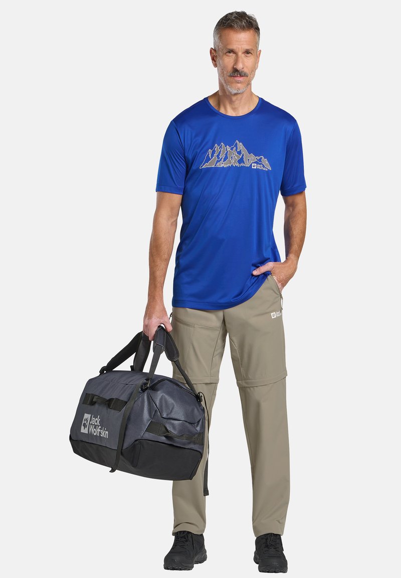 Blauw sport t-shirt met berggraphic, beige cargobroek en zwart/grijze sporttas met logo. Lichtgewicht, casual ontwerp, praktisch voor buitengebruik.