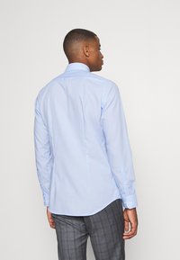 Camicia a maniche lunghe azzurro chiaro con colletto classico, polsini con bottone e dettaglio di piega sulla schiena. Realizzata in un tessuto morbido, con vestibilità su misura.