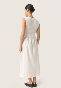Witte geribbelde tanktop met een aansluitende top en een vloeiende, geplooide midi rok. Draagt met zwarte flats, gezien van achteren.