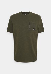 Olivově zelené tričko s krátkým rukávem vyrobené z měkké látky, které má kapsu na zip na prsou a malé černé logo Nike na kapse.