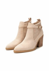Botas de tobillo de ante beige con punta afilada, recortes decorativos y una correa con hebilla. Cuenta con un tacón de madera apilada.