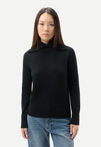 Svart ribbstickad tröja med hög krage och horisontella ränder på kragen, kombinerad med ljusblå denimjeans.