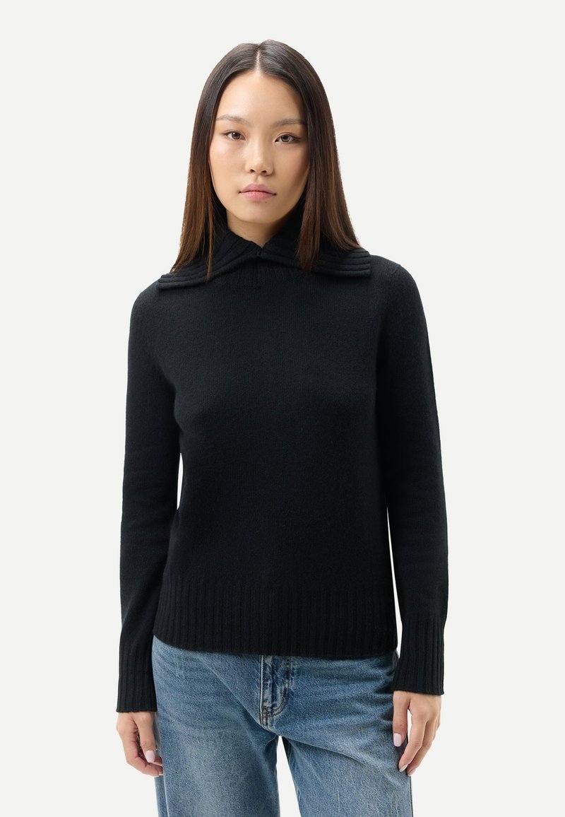 Svart ribbstickad tröja med hög krage och horisontella ränder på kragen, kombinerad med ljusblå denimjeans.