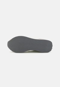 Sneaker sole in gray rubber with a zigzag tread pattern, featuring a slight curve at the edges and minimalistic design elements.