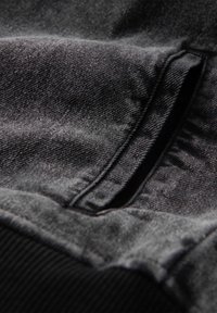 Primo piano di una tasca di giacca in denim nera con cuciture visibili e tessuto strutturato sotto luce naturale.
