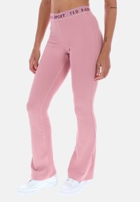 Różowe dzwonowate spodnie treningowe z teksturowanym pasem, na którym w czerni znajduje się napis "TED BAKER SPORT", w połączeniu z białymi butami sportowymi.
