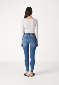 Skinny blue denim jeans with a high waist, faded details, and frayed hems, paired with a light grey long-sleeve top.
