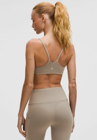 Sujetador deportivo de color beige claro con tirantes finos, diseño de espalda redondeada y tela suave. Combinado con leggings de talle alto a juego.
