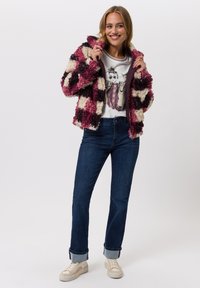 Zachte jas met ruitpatroon in bordeauxrood, crème en donkerpaars, gecombineerd met een grafisch t-shirt en donkerblauwe jeans.