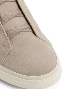 Beżowe zamszowe sneakersy z płaskimi sznurowadłami, okrągłym czubkiem i gumową podeszwą. Charakteryzują się detalami w postaci przeszyć oraz gładką teksturą.