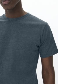 T-shirt gris foncé à manches courtes avec un col rond, fabriqué en tissu texturé, montrant un gros plan de l'épaule et du haut de la poitrine.