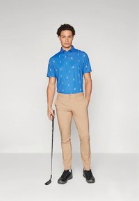 Blå pikétröja med golfmotiv, matchad med beige byxor och svarta skor. Tröjan har en klassisk krage och korta ärmar.