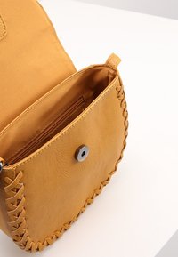 Borsa a mano gialla in pelle con dettagli intrecciati, chiusura a scatto magnetico e interno in tessuto liscio con una tasca con zip.