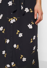 Blumenkleid mit dunkelblauem Hintergrund, weißen Blumen mit gelben Akzenten, Knopfleiste und einem weichen, strukturierten Stoff.