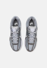 Nike sportbačiai su pilku ir šviesiai mėlynu austu viršumi, pilkiais akcentais, baltais raišteliais ir paminkštintu padu. Logotipas ant liežuvėlio ir vidpadžio.