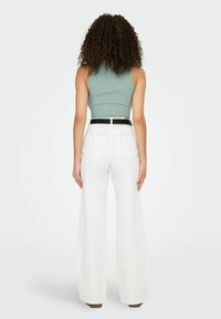 Witte high-waisted broek met wijde pijpen, voorzien van achterzakken, gecombineerd met een groene cropped tanktop. Gladde textuur, minimalistisch ontwerp.