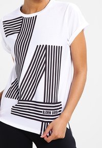 Hvid T-shirt med et iøjnefaldende sort linjært grafikdesign. Korte ærmer, rund halsudskæring, blødt stof med brandnavnet "BJÖRN BORG" nederst.