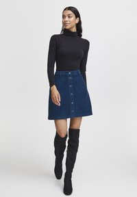 Zwarte lange mouwen coltrui, gecombineerd met een donkerblauwe corduroy A-lijn rok met knopen aan de voorkant en een gestructureerde afwerking. Zwarte kniehogere laarzen.