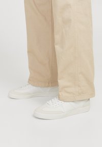 Weiße Sneaker aus strukturiertem Leder und Mesh-Einsätzen, mit einem Low-Top-Design und Schnürverschluss, getragen mit hellbeigen Hosen.