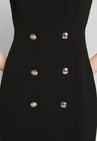 Schwarzes Stoffkleid mit passgenauem Design, das sechs silberne runde Knöpfe entlang der Vorderseite und eine glatte Textur aufweist.