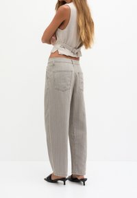 Striped, high-waisted pants in light gray with a relaxed fit. Features two back pockets and a smooth texture. Worn with a simple sleeveless top.