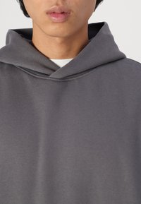 Grå hettegenser laget av myk stoff, med rund hals og subtile søm detaljer. Minimalistisk design, uten mønstre.