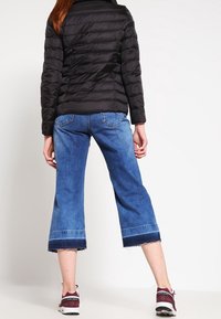 Veste matelassée noire, culottes en denim bleu taille courte avec un ourlet effiloché, et chaussures de sport bordeaux avec des semelles blanches. Design clair et structuré.