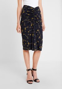 Jupe crayon marine avec un motif de fleurs jaunes, dotée de détails froncés à la taille et d'un tissu lisse et extensible. Sandales à talons hauts noires.