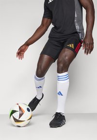 Maglietta sportiva nera con accenti grigi, pantaloni corti neri con dettagli rossi e oro, calze bianche con righe blu, scarpini da calcio neri e un pallone da calcio multicolore.